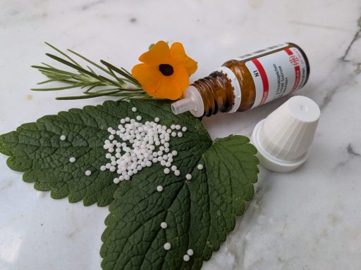 Klassische Homöopathie Braune Flasche mit Homöopathie-Kügelchen, grünen Blättern und einer orangefarbenen Blume.